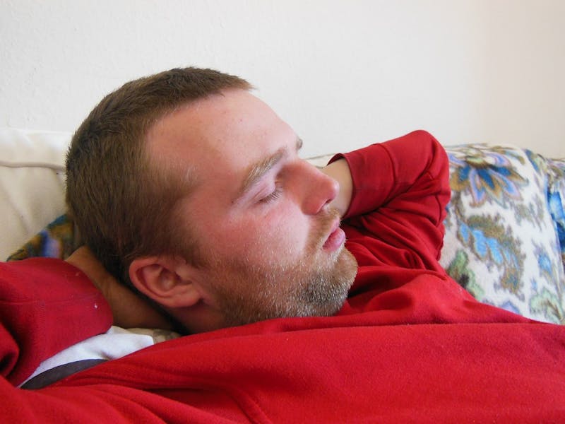 there is a man laying on a couch with hands behind head and eyes closed