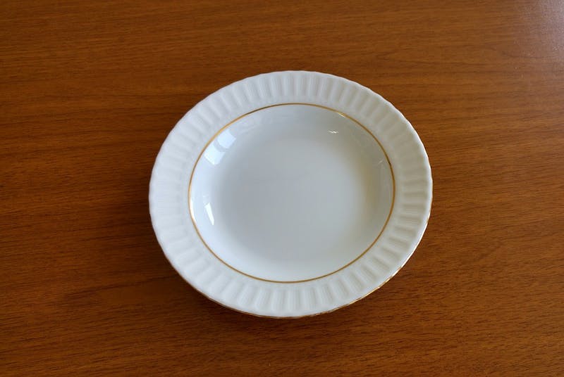 there is a empty white plate with a gold rim on a wooden table