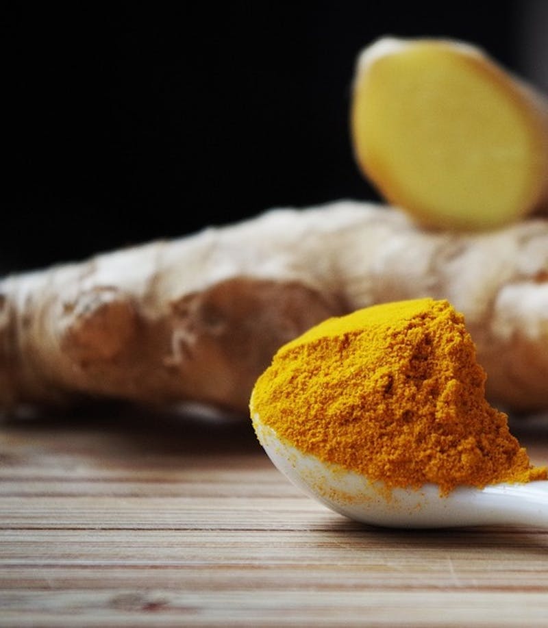 there is a spoon with tumeric and a piece of ginger on it