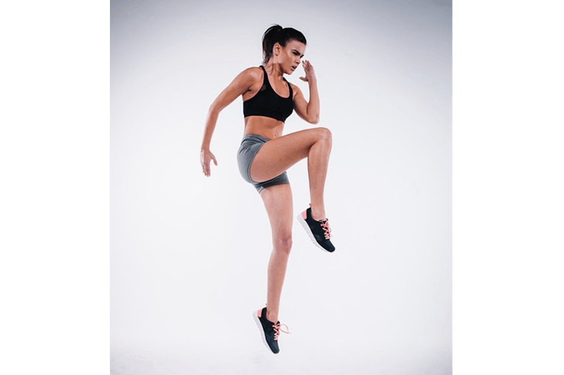 woman in a black sports bra top and grey shorts jumping in the air