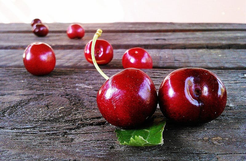 there are cherries on a wooden table with leaves on it