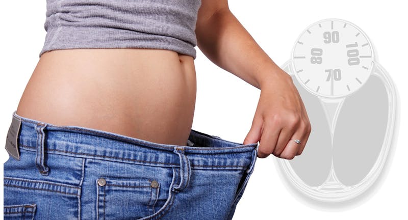 woman in jeans holding them out with a weight scale in the background