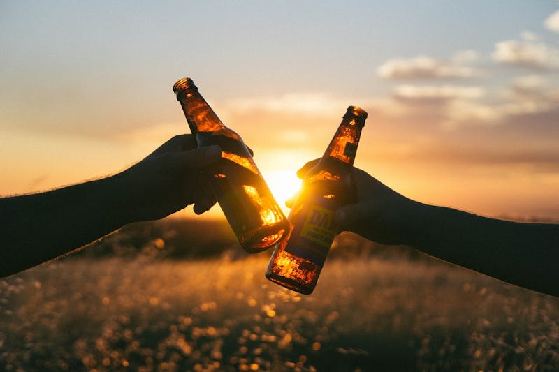 two people holding beer bottles in front of a sunset