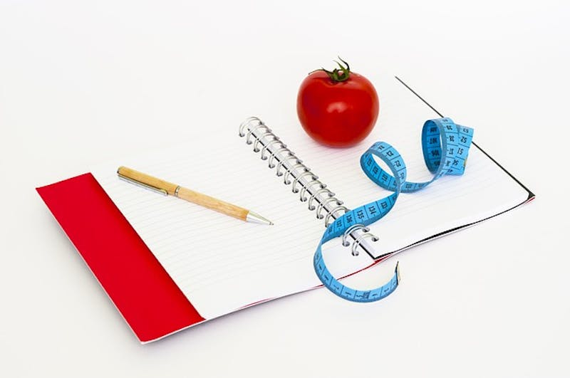 notebook with a measuring tape and a pencil next to a apple
