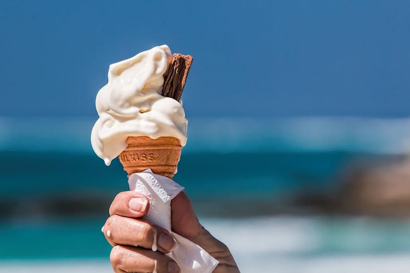 close up of someone holding a cone of ice cream on the beach