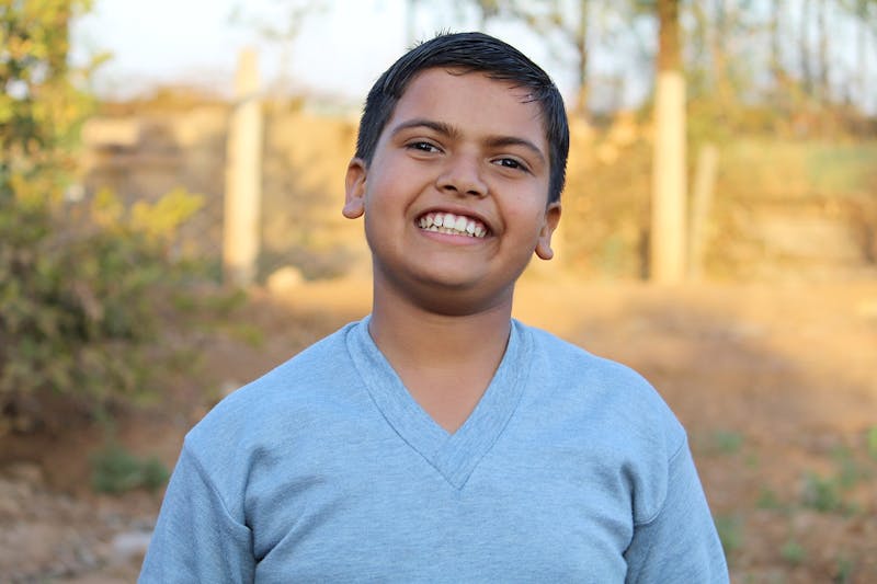 smiling boy in a blue shirt standing in a field with trees