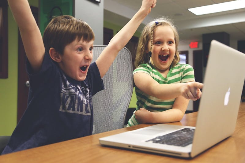 there are two children sitting at a table with their hands in the air