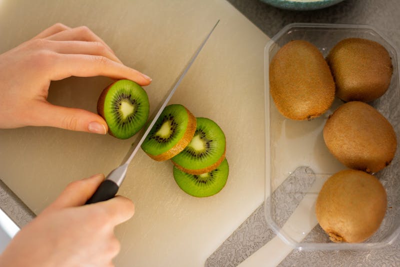 someone cutting up a kiwi on a cutting board with a knife