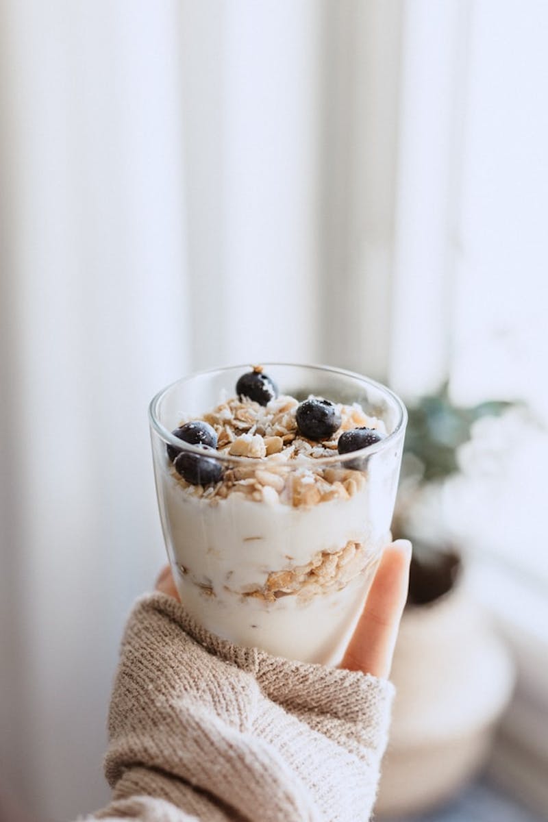 someone holding a glass of yogurt with blueberries in it