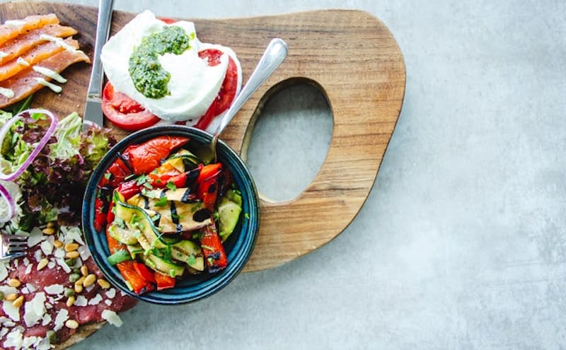 there is a wooden cutting board with a salad and other foods