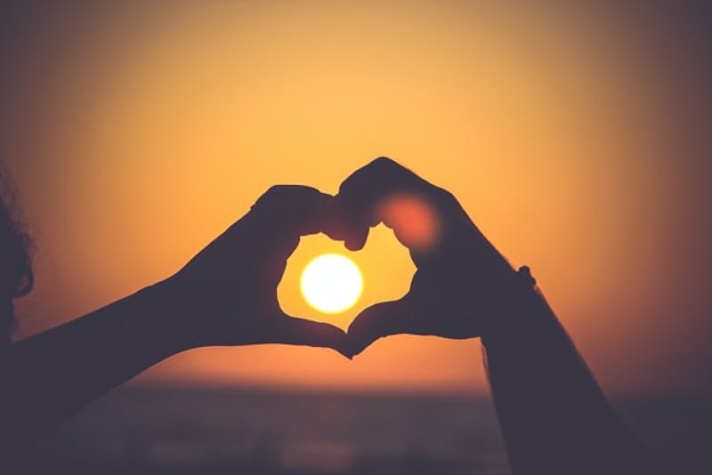 someone making a heart shape with their hands at sunset