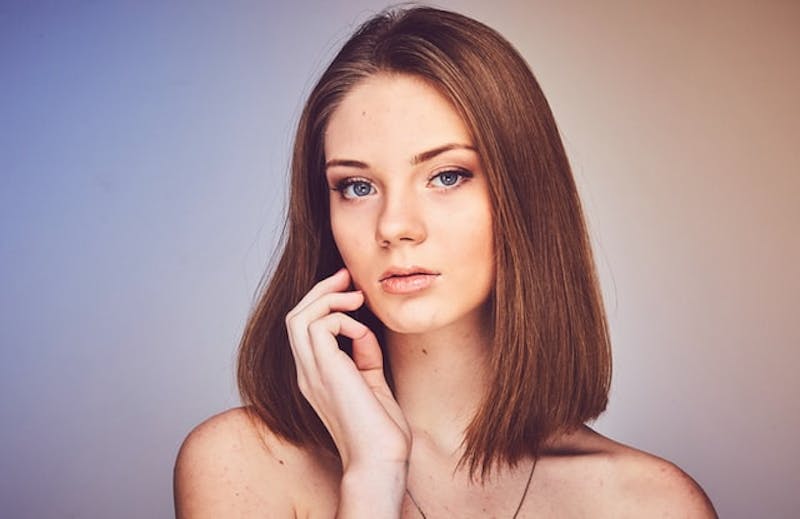 woman with a necklace and her hand touching her face posing for picture
