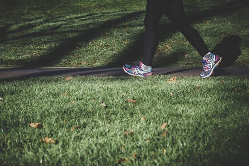 close up of a person's lower legs walking on a sidewalk with tennis shoes
