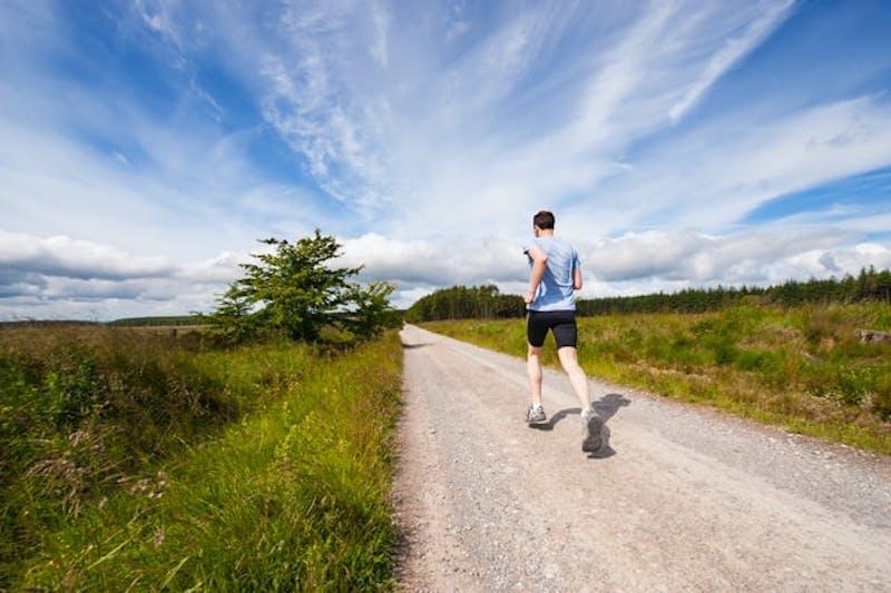 a man running on a dirt road in the middle of a field