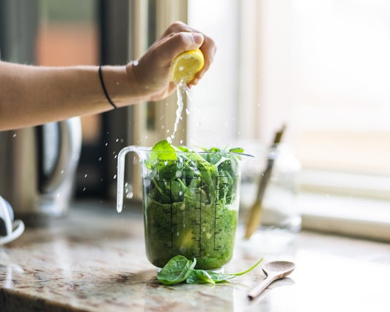 someone is squeezing a lemon into a blender filled with spinach