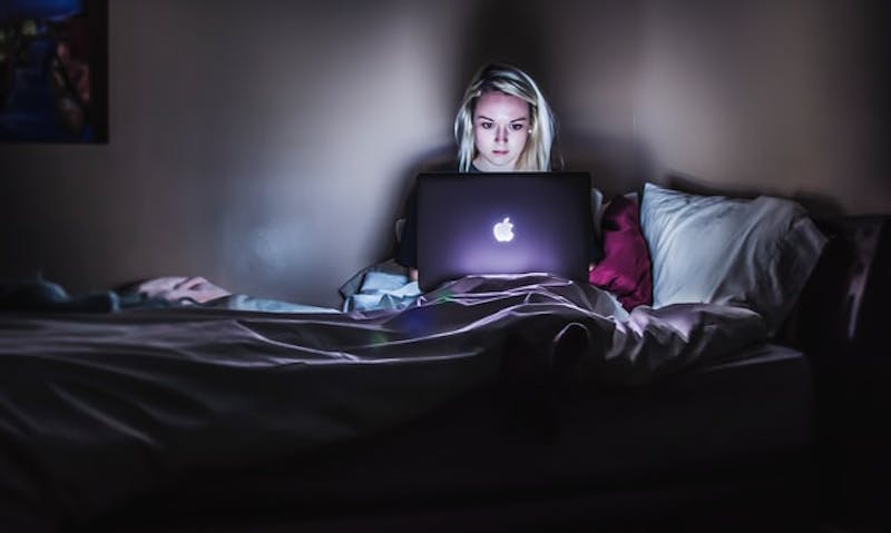 woman sitting in bed with laptop in dark room with light on 2