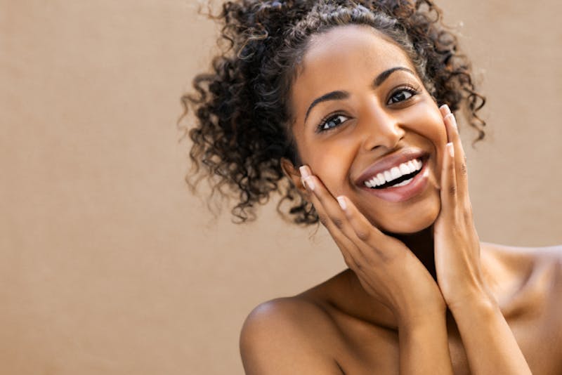 smiling woman with curly hair and hands on face