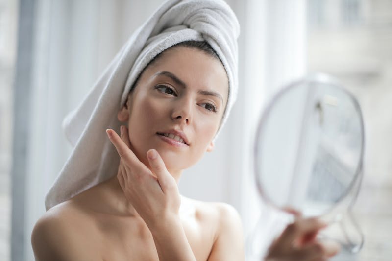 woman with towel on head looking at herself in mirror