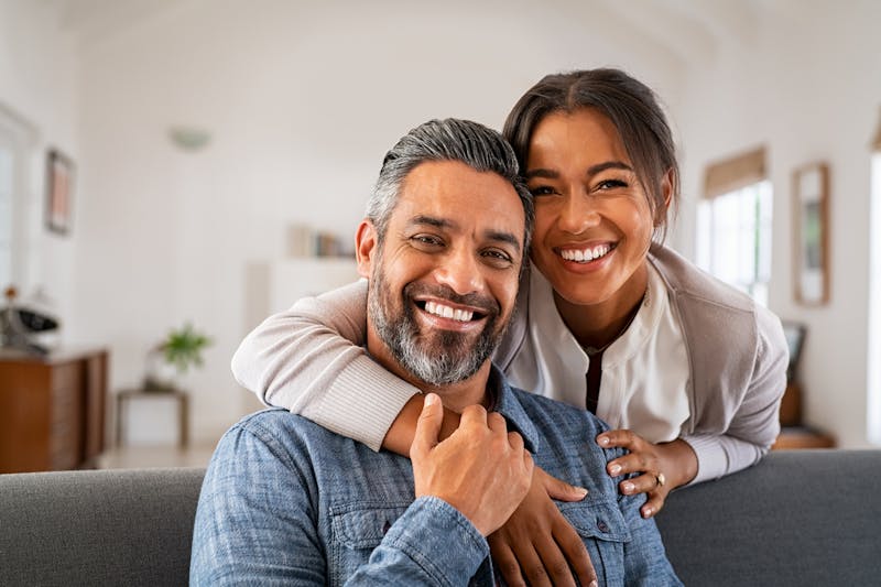 smiling couple sitting on couch in living room with arms around each other