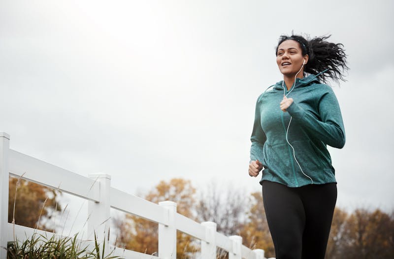 woman running on a path in a park with a white fence