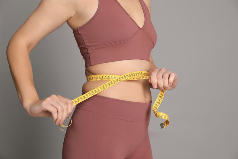 woman in a sports bra top holding a measuring tape across waist