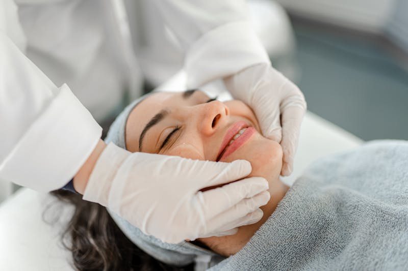 smiling woman having face inspected by doctor in white surgical gloves
