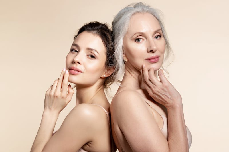 a young woman with an older woman posing for a picture in front of a beige background back to back