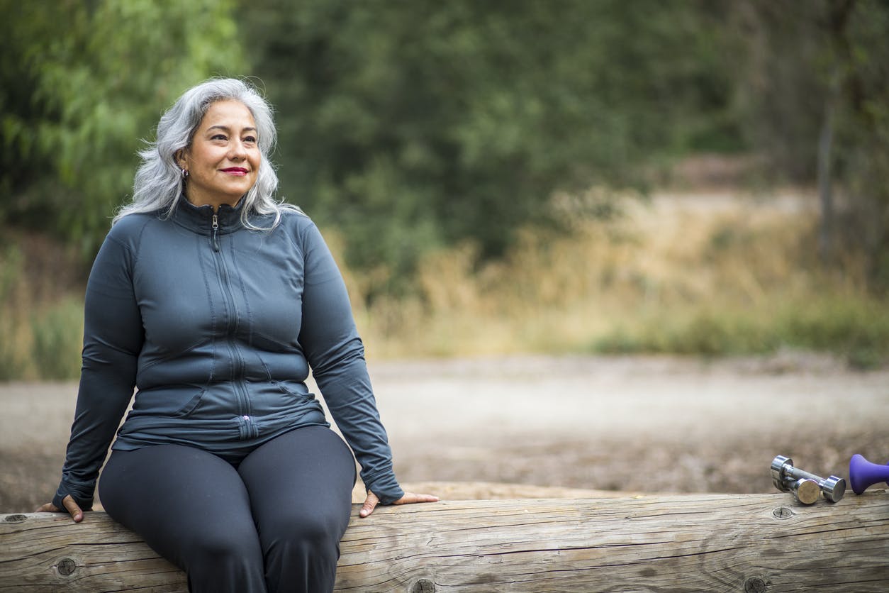 a woman sitting on a log by a trail with a set of weights to her side