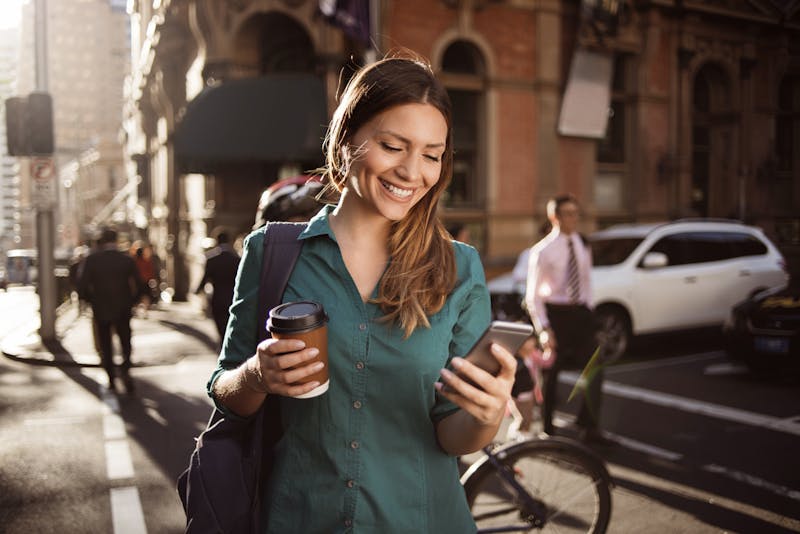 woman holding a cup of coffee in one hand and looking at her phone in the other