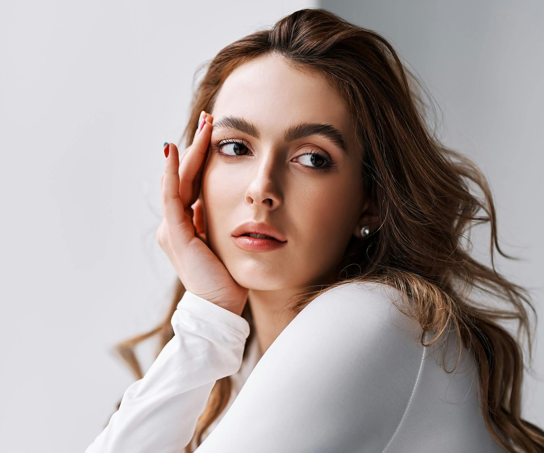 Woman in white top resting her hand on her face