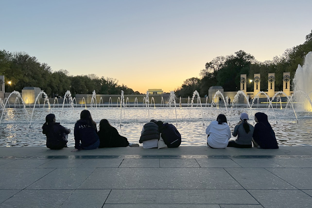 A groups of students with their backs to the camera at sunset overlooking the fountain and the World War II Memorial in Washington, DC