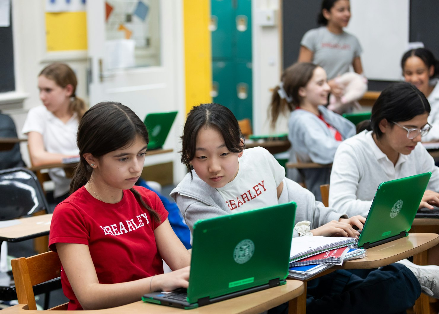 Two middle school students sitting at their desks, working on their laptop computers, helping each other with their assignment.