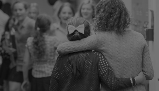 Two students with their backs to the camera but with their arms around each other.