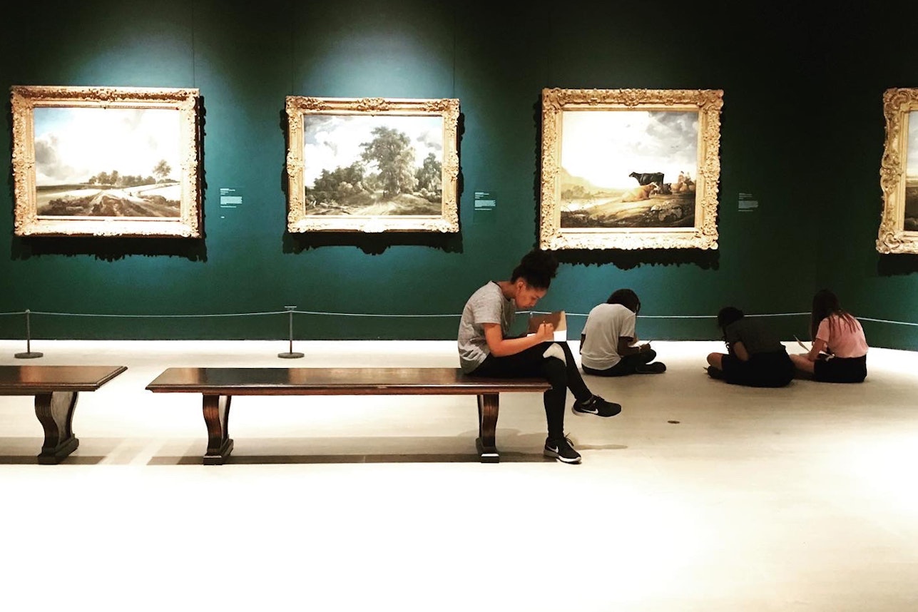 A student sitting on a bench at the Metropolitan Museum of Art focusing on her own drawing