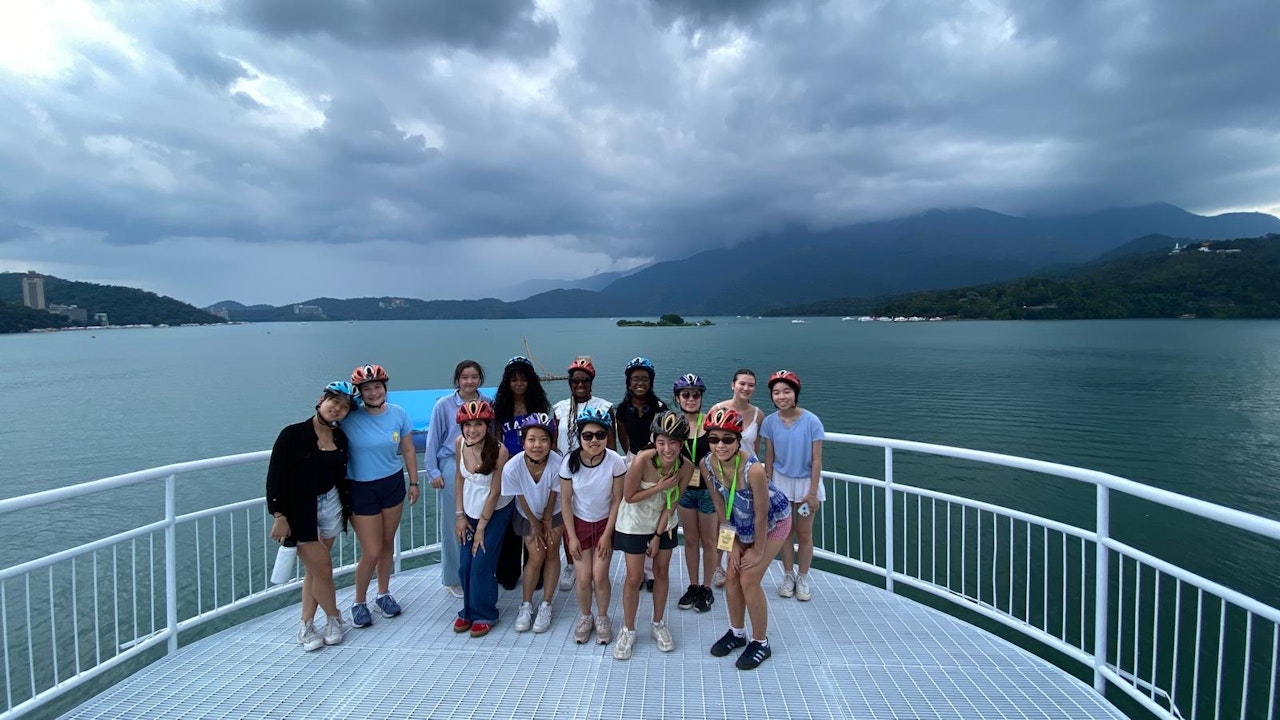 Upper School students posing as a group with bike helmets on in front of a picturesque shoreline in Taiwan