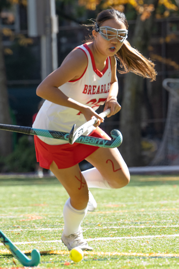 A field hockey player making a diving play for the ball against two opponents.