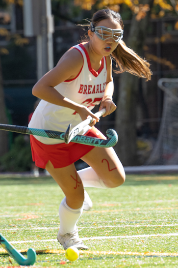 A field hockey player making a diving play for the ball against two opponents.