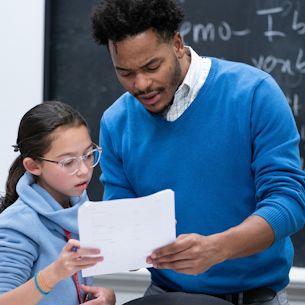 A male teacher looking over in-class work with a middle school student.