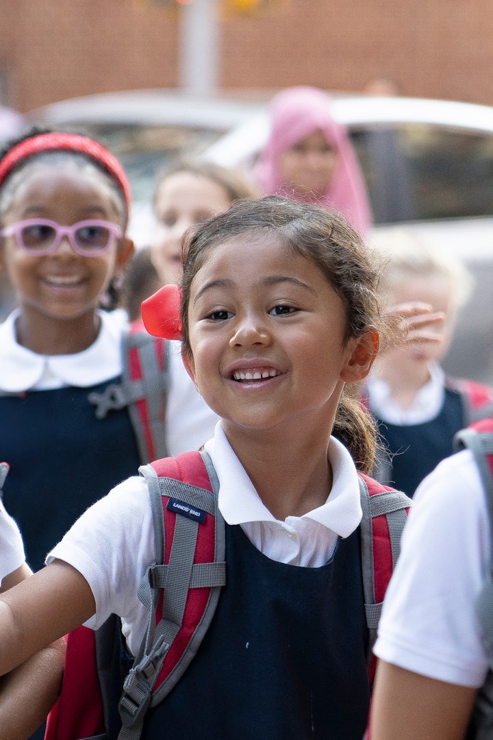 A lower school student on her way into school, smiling and carrying her backpack