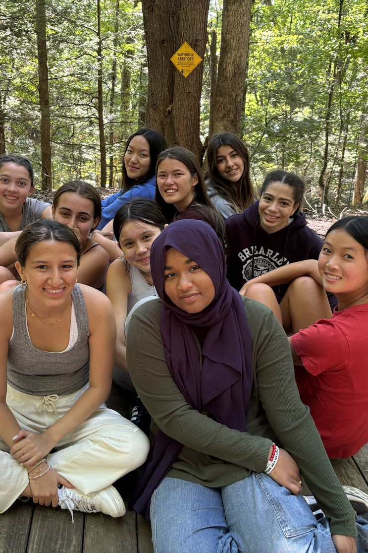 A group of seniors sitting on a large wooden plank in the woods during a school trip