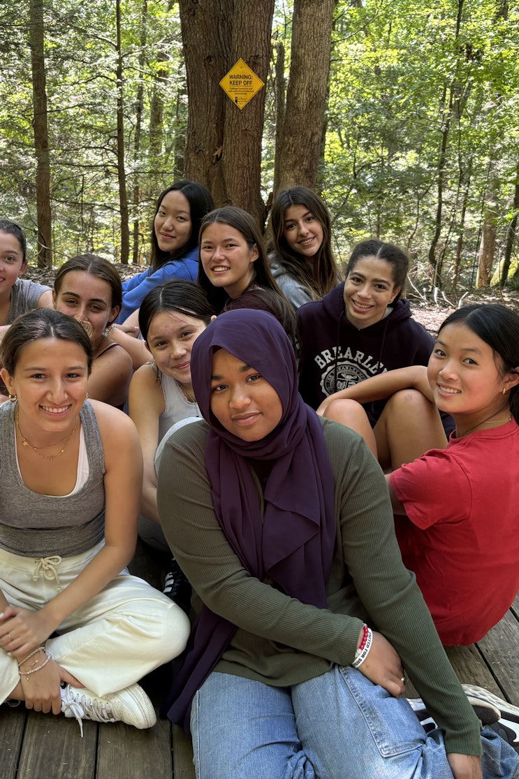 A group of seniors sitting on a large wooden plank in the woods during a school trip