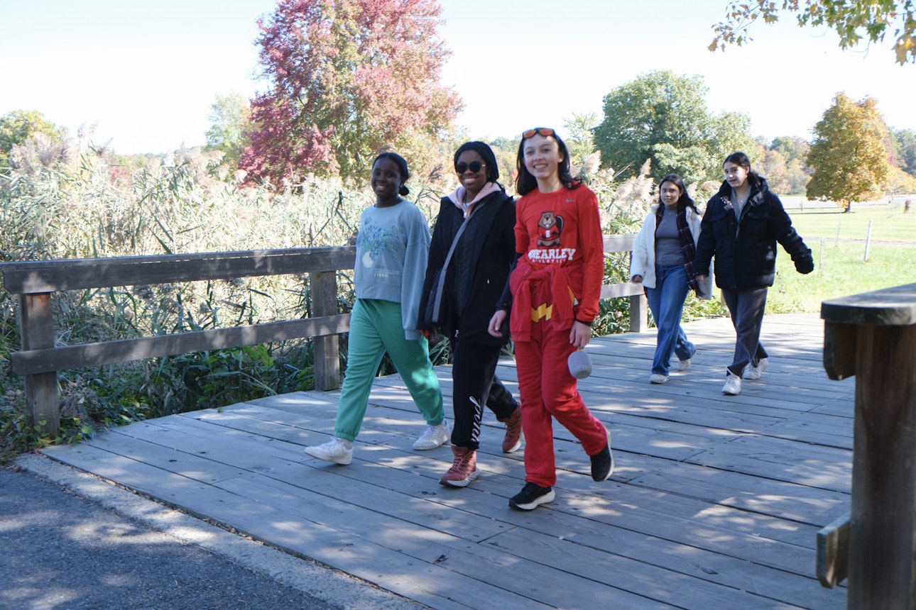Students at Mountain Day taking a hike across a wooden bridge with beautiful fall foliage in the background..