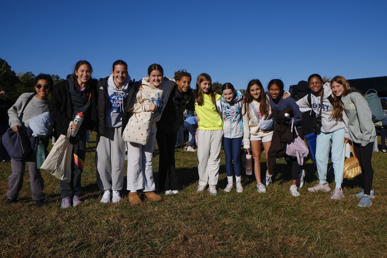 A group of middle school students posing for a photo all in a row, smiling with their arms around each other.