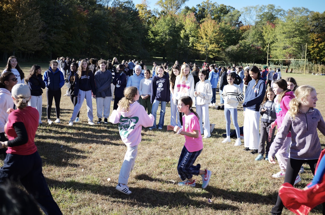 Upper School students participating in a group activity involving students in a circle around two girls in the middle on Mountain Day.