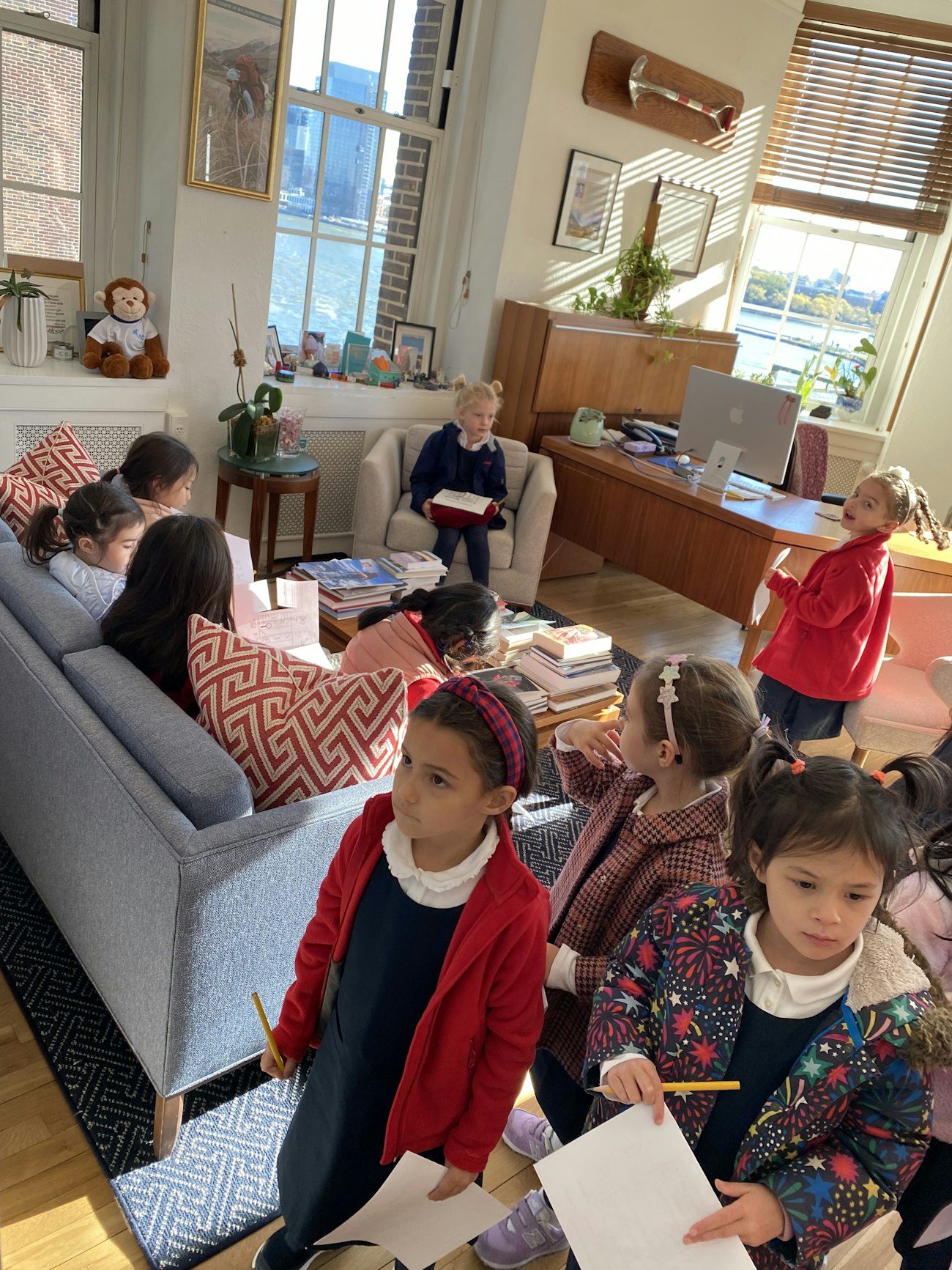 Kindergarten students take over the head of school's office, sitting on the couch and chairs.