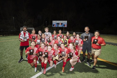 A team photo of the varsity soccer team and their coaches holding the NYSAIS championship trophy.