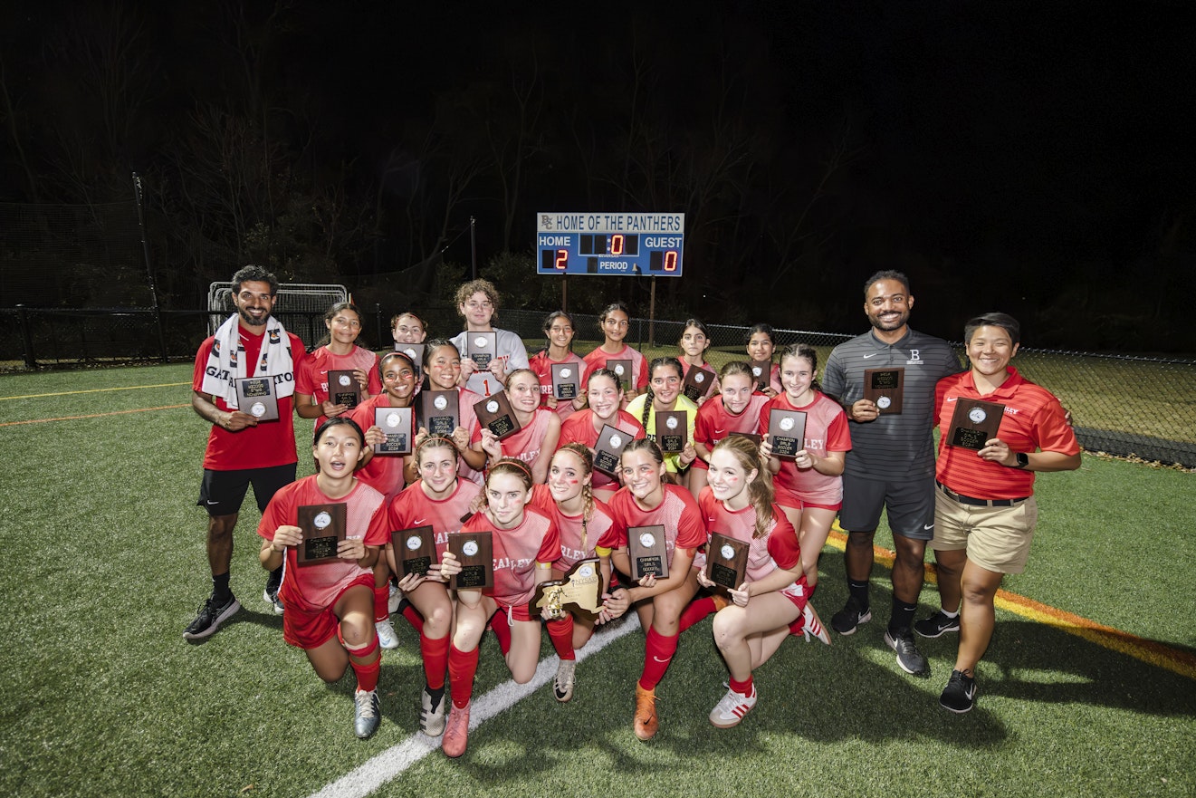 A team photo of the varsity soccer team and their coaches holding the NYSAIS championship trophy.