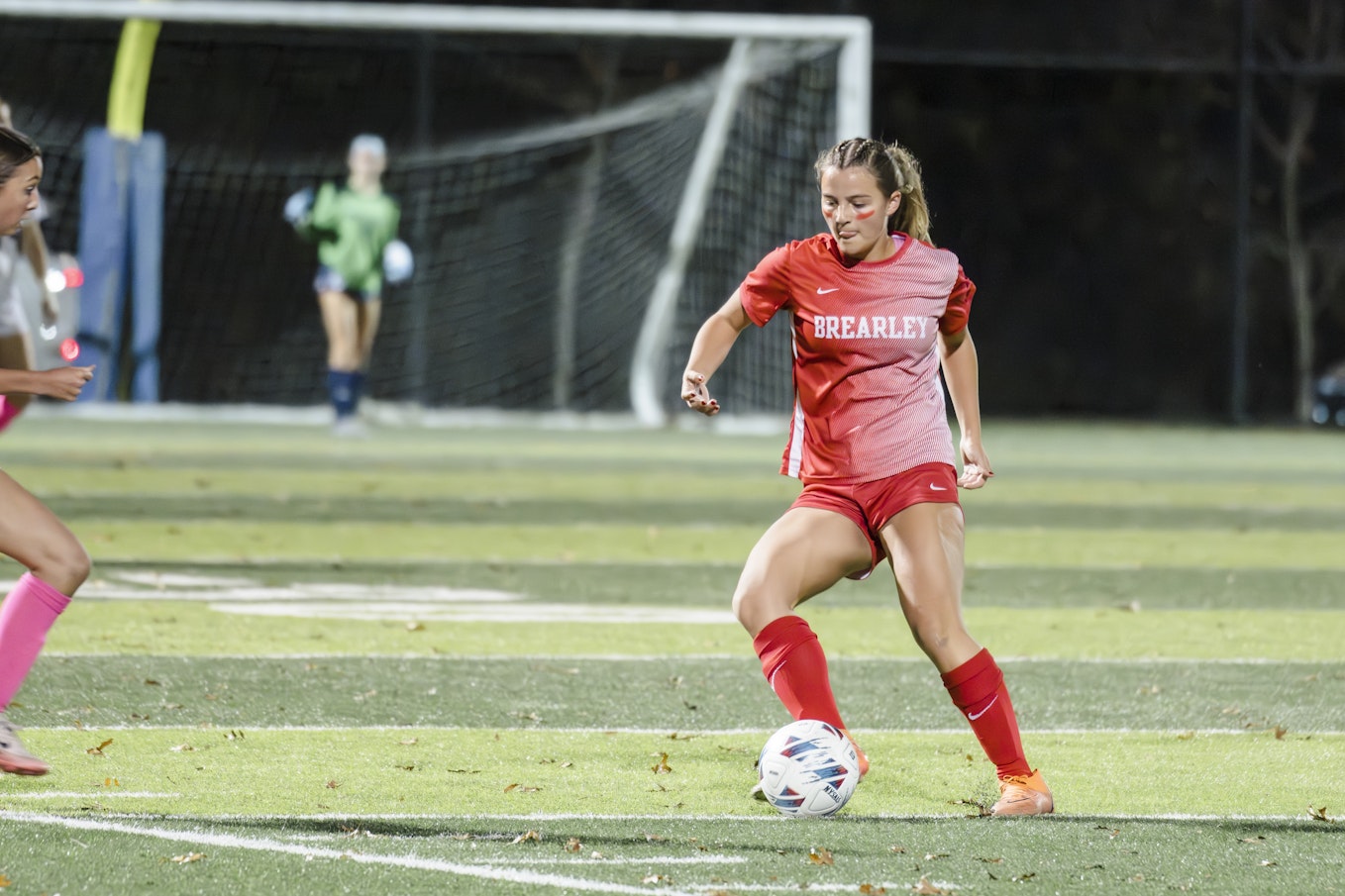 A member of the varsity soccer team dribbling the ball on the pitch during the league championship game.