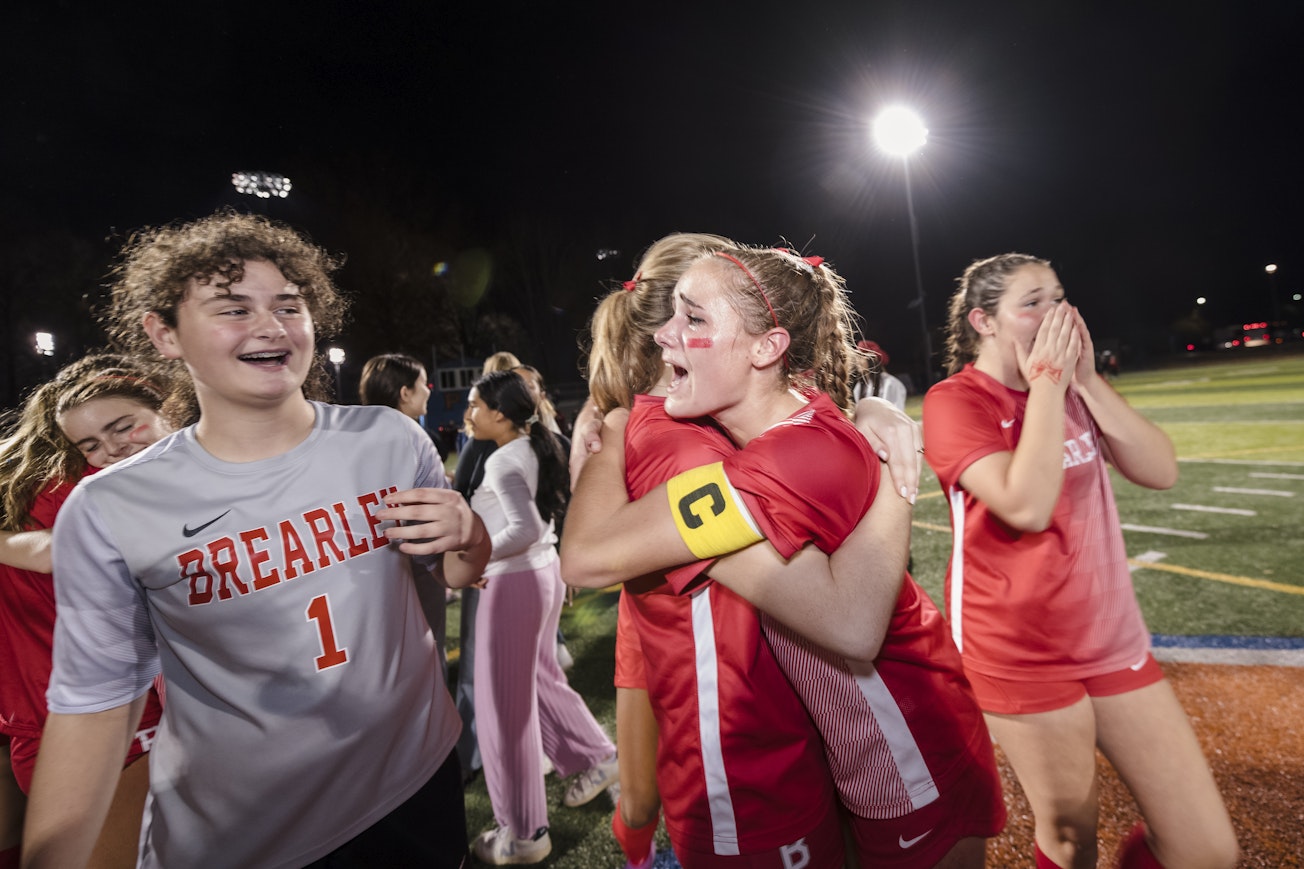 Members of the team celebrating their league championship win by hugging each other and clapping their hands over their mouths in joy.