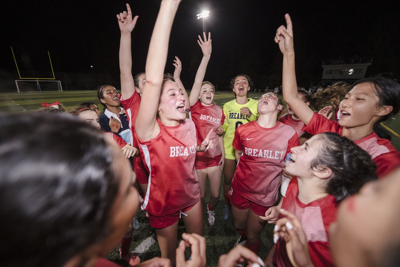 Members of the varsity soccer team celebrating their league championship victory by singing loudly and raising their hands in the air.